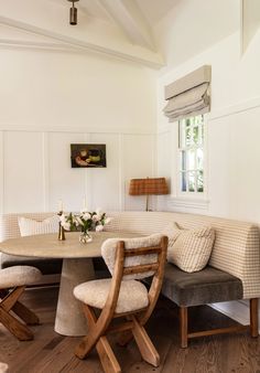 a dining room table with two chairs and a bench in front of it, next to a window