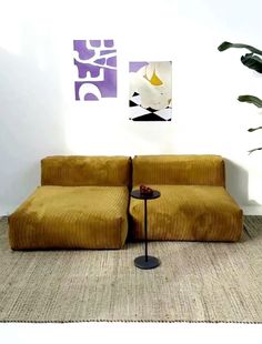 a brown couch sitting next to a table on top of a carpeted floor in front of a white wall