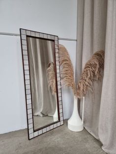 a tall mirror sitting on top of a white table next to a vase filled with feathers