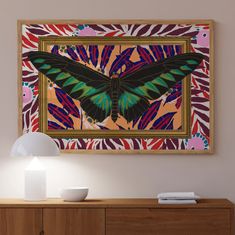 a colorful butterfly painting hanging on the wall above a wooden dresser with two white lamps