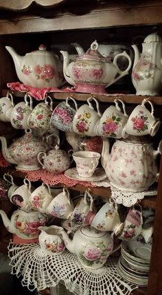 a shelf filled with lots of different kinds of tea pots and saucers on top of lace doily