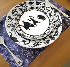 two plates with black and white designs on them sitting on a table next to utensils