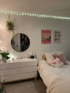 a bedroom with white furniture and lights on the wall above the bed, along with plants