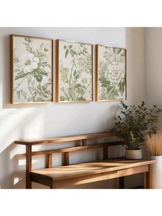 a wooden bench sitting in front of two paintings on the wall next to a potted plant