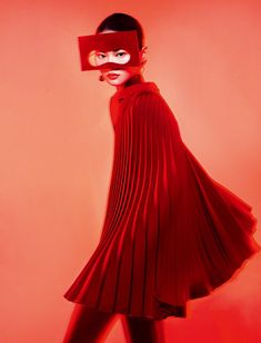 a woman in a red dress with a mask on her face, standing against an orange background