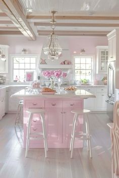 a white and pink kitchen with two stools in front of the island, an oven and refrigerator