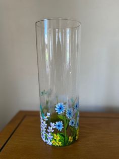 a glass with flowers painted on it sitting on top of a wooden table next to a wall