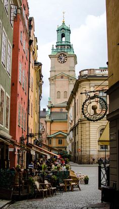 a clock tower towering over a city street filled with buildings and people sitting at tables