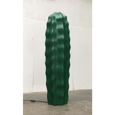 a large green vase sitting on top of a cement floor next to a white wall