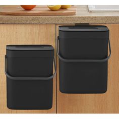 two black trash cans sitting next to each other on top of a wooden countertop