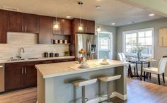 an open kitchen and dining room with wood flooring, white counter tops and bar stools