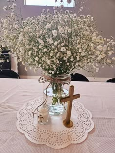 a vase filled with white flowers and a wooden cross on top of a doily