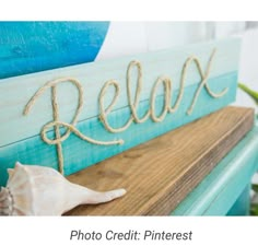 a wooden sign that says relax on top of a shelf next to a sea shell