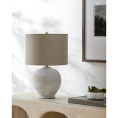 a table lamp sitting on top of a wooden shelf next to a framed photograph and potted plant