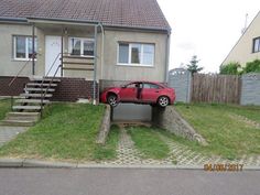 a red car parked in front of a house on the side of a road with stairs leading up to it