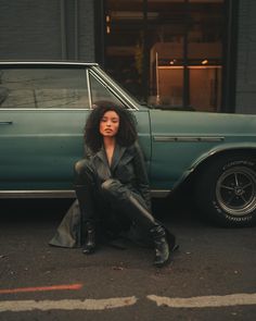 a woman sitting on the ground in front of a car with her legs crossed and wearing black boots