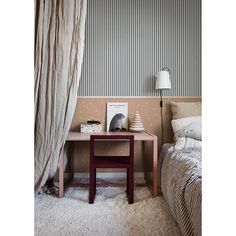 a room with a bed, table and lamp on it in front of a striped wall