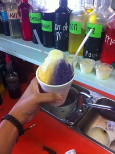 a person holding an ice cream cone in front of a sink filled with liquids