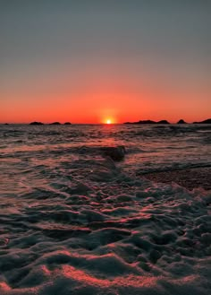 the sun is setting over the ocean with waves coming in to shore and an orange glow on the horizon