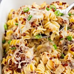 a spoon full of pasta with meat and cheese on it is being lifted from the casserole dish