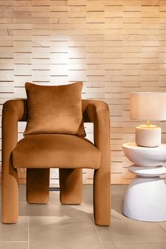 a brown chair sitting next to a white vase and lamp on top of a tiled floor