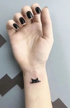 a small black cat tattoo on the wrist