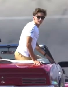 a man riding on the back of a red convertible in front of a red car