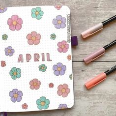 an open notebook with flowers and the word april written on it next to some markers