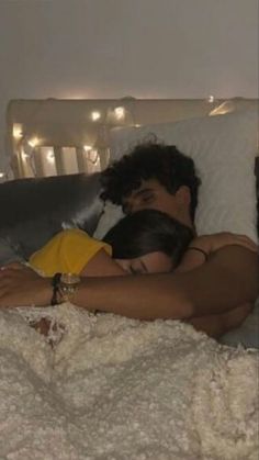 a man and woman laying in bed with their arms around each other, cuddling