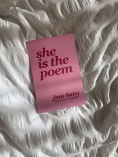 a pink book sitting on top of a white sheet covered bed next to a pillow