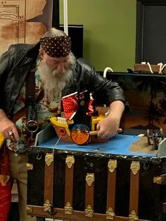 a man with a long white beard is looking at a pirate ship in a trunk