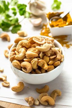 a white bowl filled with cashews on top of a wooden table next to other nuts