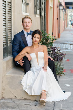 a man and woman are sitting on the steps in front of a building, posing for a photo