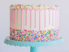 a birthday cake with sprinkles and frosting on a blue stand against a white wall