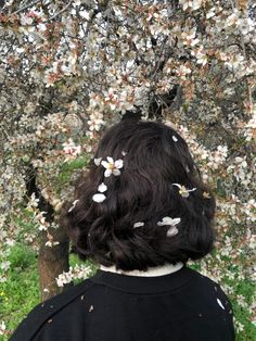 the back of a woman's head with white flowers on her hair in front of a flowering tree