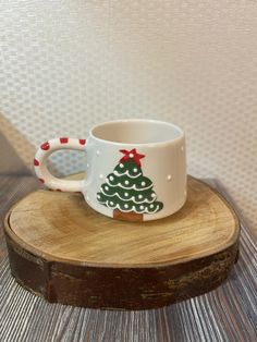 a coffee cup with a christmas tree painted on it sitting on top of a wooden stand