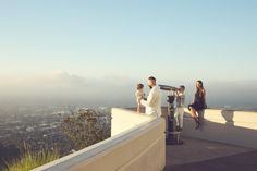 a group of people standing on top of a building next to a parking meter with a city in the background