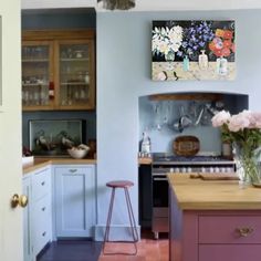 a kitchen with blue walls and purple cabinets, pink stools and flowers on the counter