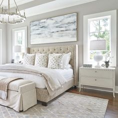 a large white bed sitting in a bedroom on top of a hard wood floor next to a window