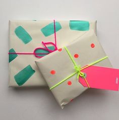 two wrapped presents are sitting next to each other on a white surface with pink and green tags