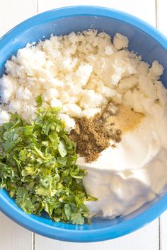 ingredients in a blue bowl including parsley, sour cream and seasoning for mashed potatoes