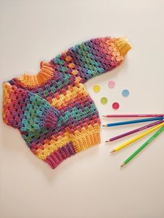 crocheted sweater and colored pencils laid out next to it on a white surface