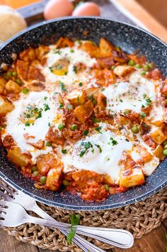 a skillet filled with meat and cheese on top of a wooden table next to eggs