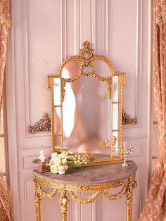 an ornate vanity with flowers and candles on it in front of a pink painted wall