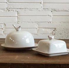 two white dishes sitting on top of a wooden table next to a brick wall,