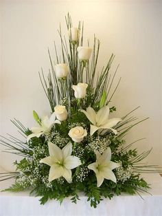 white flowers and greenery are arranged in a centerpiece on a tableclothed cloth