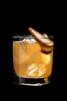 an apple and cinnamon drink in a glass with ice cubes on the rim, against a black background