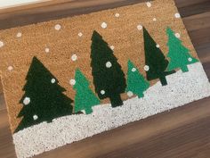 a door mat with trees painted on it in front of a wooden floor and white snowflakes