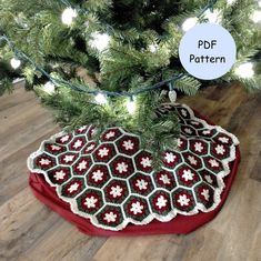 a crocheted christmas tree skirt on top of a red round pillow under a pine tree