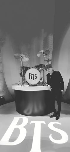 a man standing next to a drum set on top of a white stage with the words bts written across it